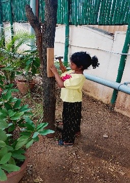 A child fixing a wooden board to a tree in the carpentry space